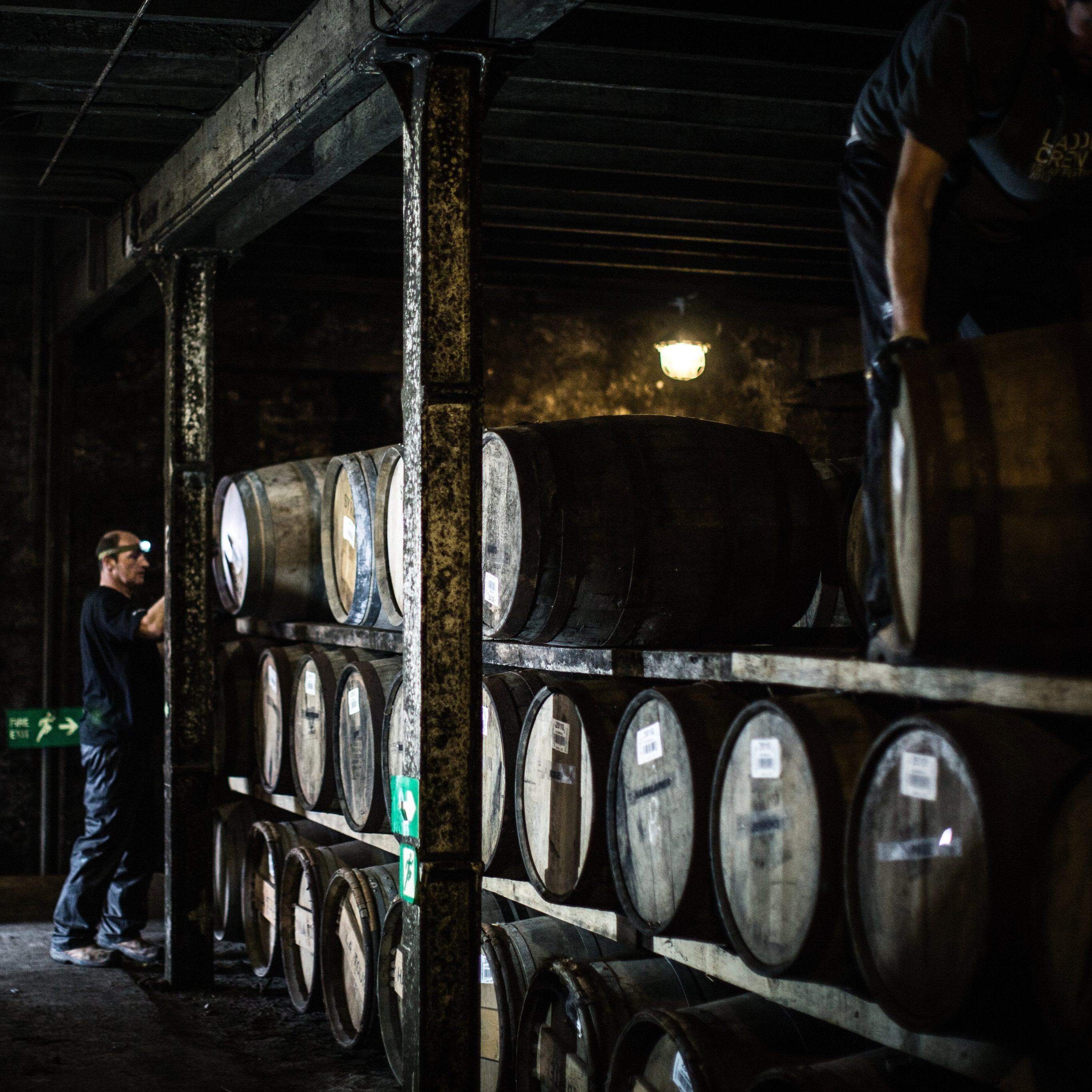 Bruichladdich Distillery team members working among stacked whisky casks in a dimly lit warehouse.