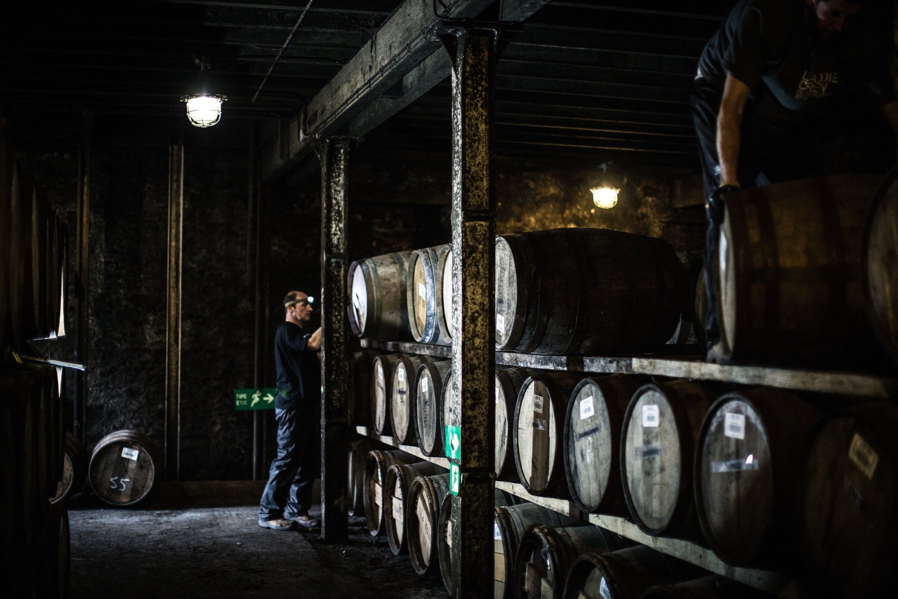 Bruichladdich Distillery team members working among stacked whisky casks in a dimly lit warehouse.